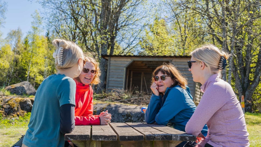 Four women laughing in a sunny outdoor environment