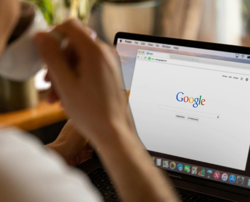 Image of person drinking a cup of coffee in front of a computer screen with Google Search on display