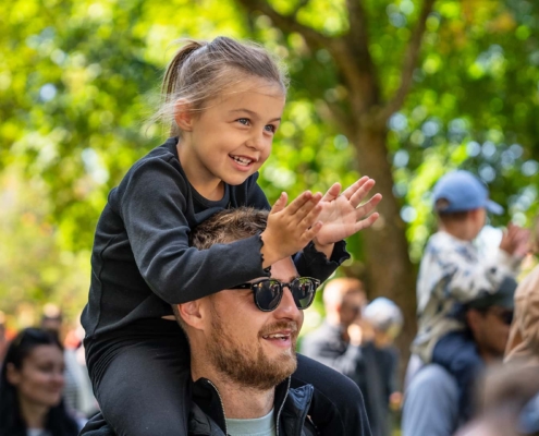 happy dad with his daughter on his shoulders looking at a performance at an event