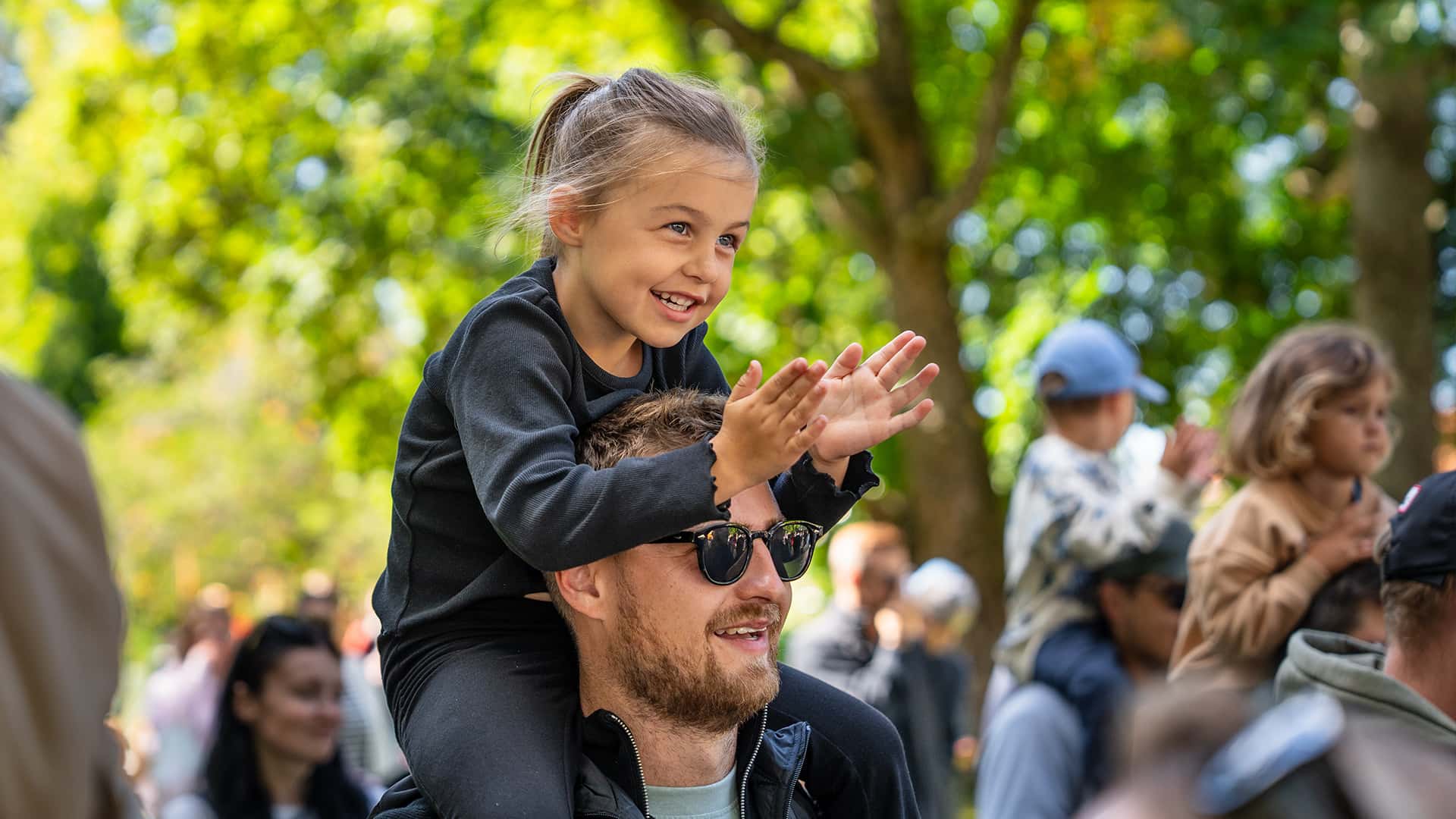 happy dad with his daughter on his shoulders looking at a performance at an event
