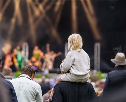child sitting on parents shoulders at a concert