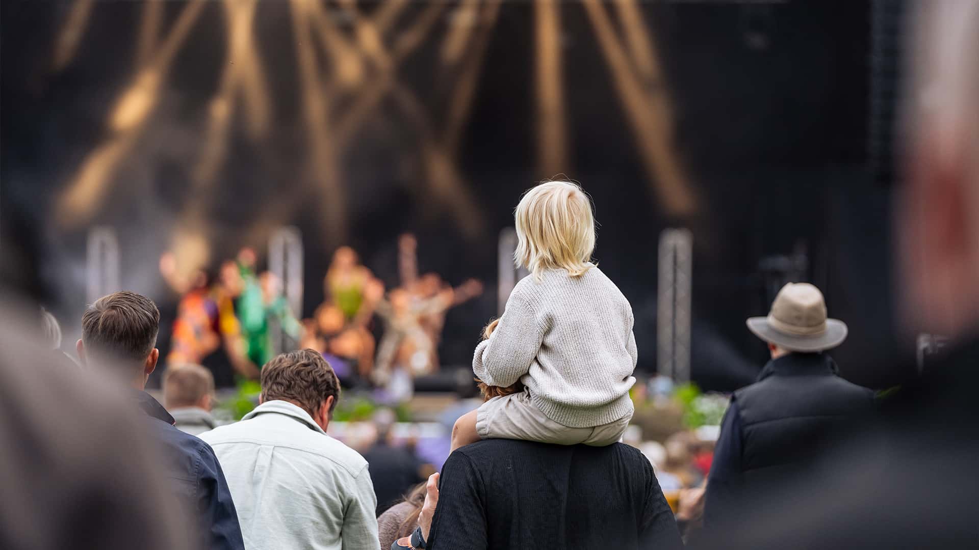 child sitting on parents shoulders at a concert