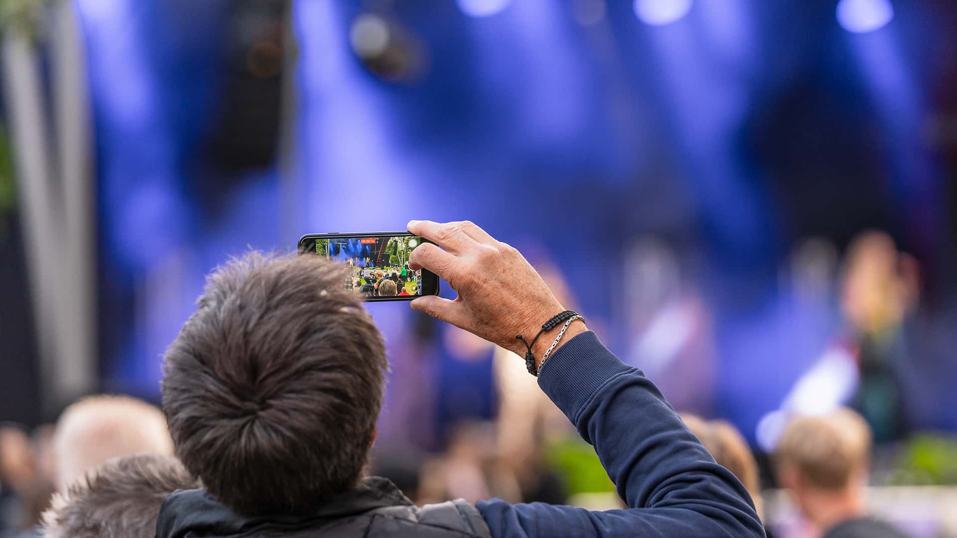 a guy filming a concert with his phone in focus