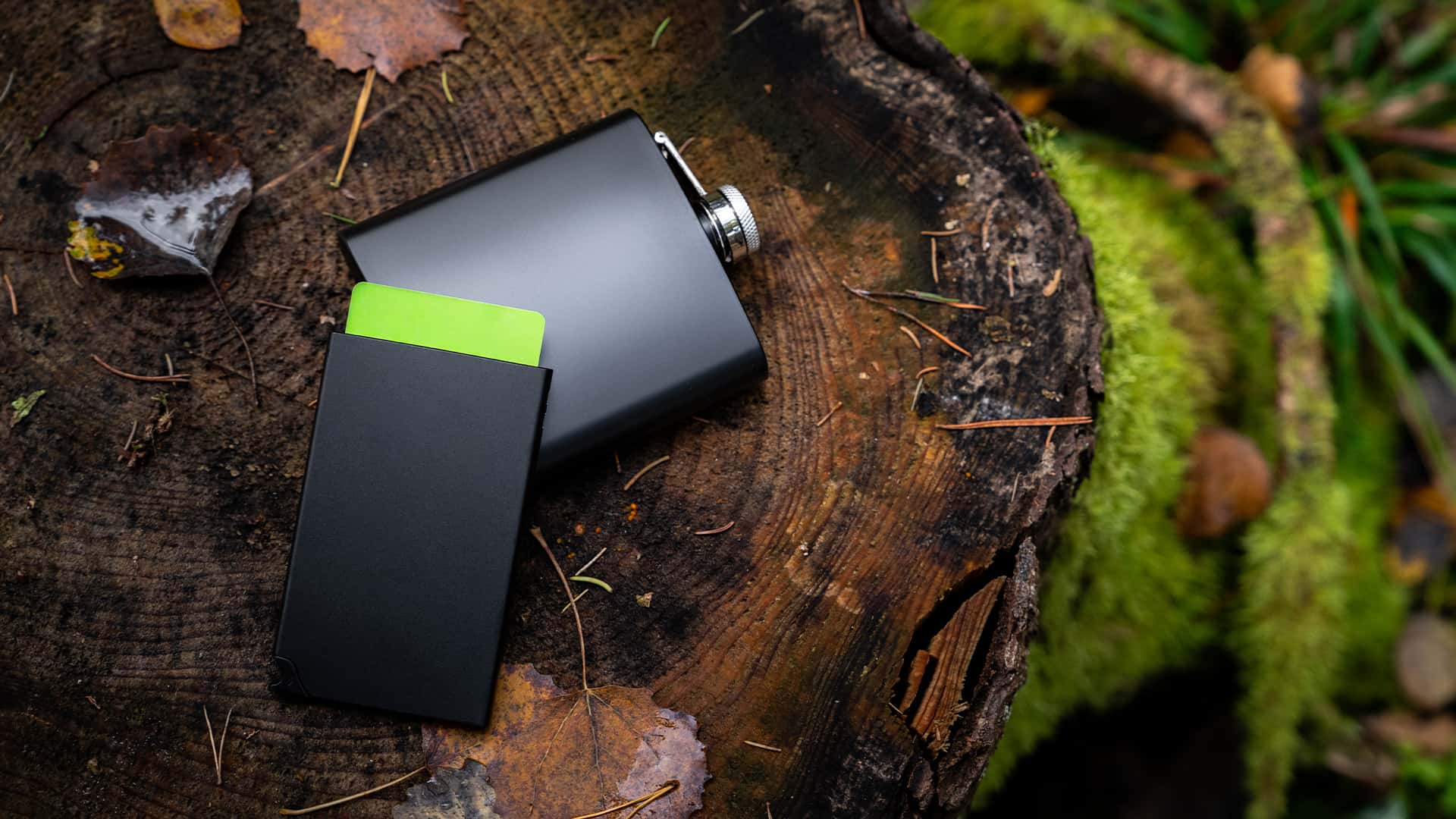 close up of a card holder with pocket flask besides it shot in a forest