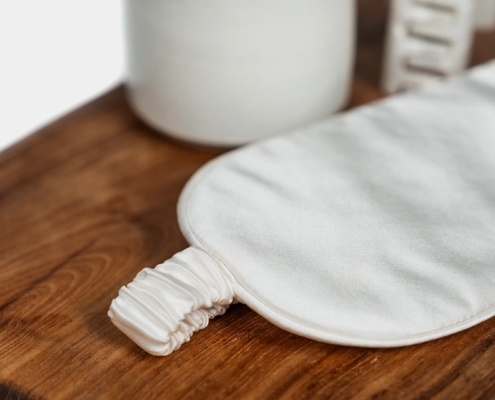 close up of a sleeping mask in silk with misc items on a stool