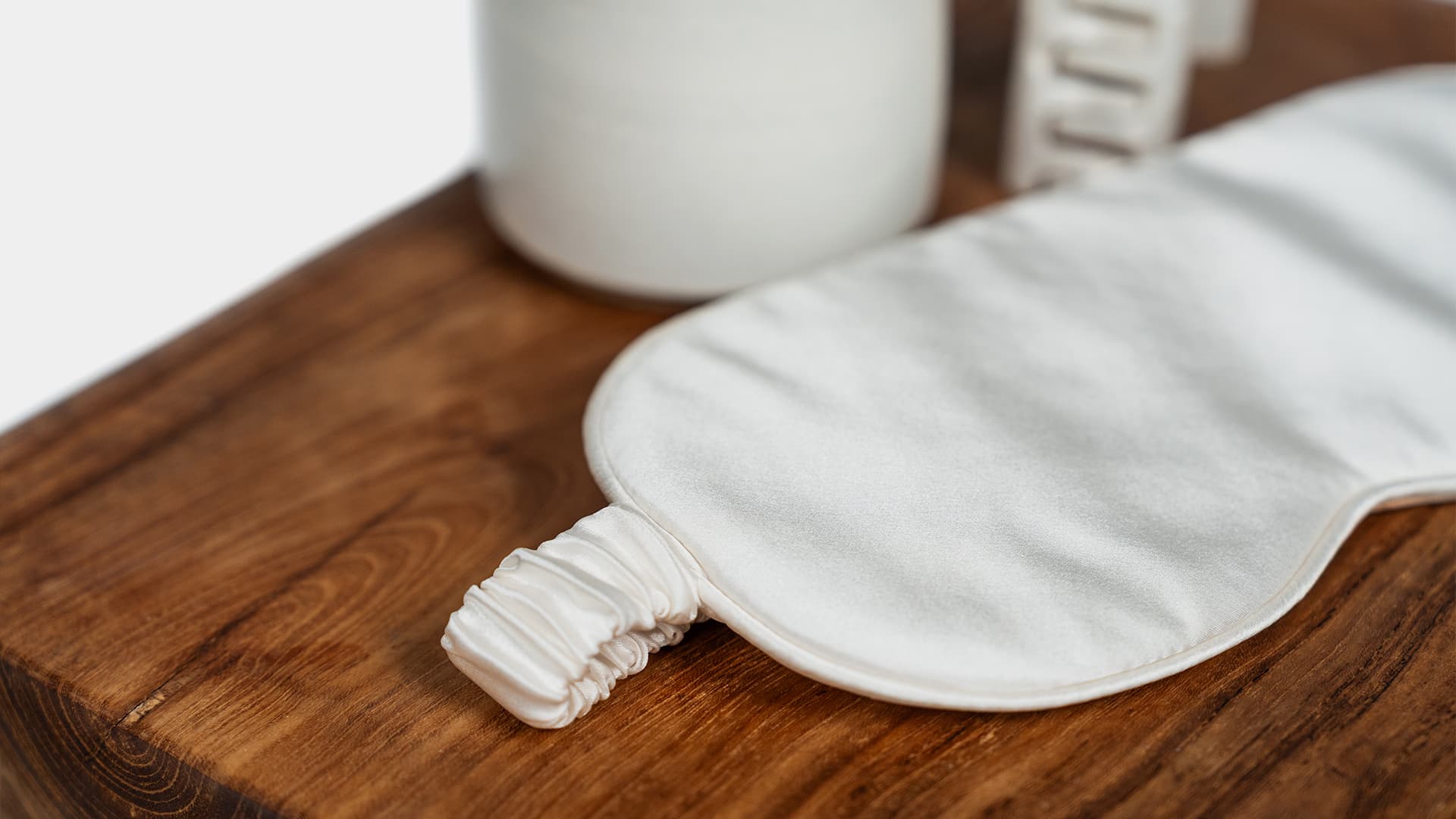 close up of a sleeping mask in silk with misc items on a stool